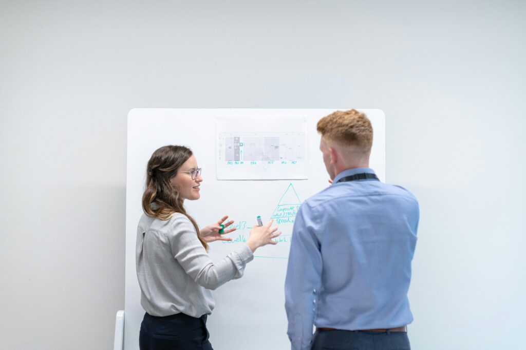pexels-photo-3862603-3862603 Two professionals discussing project plans at whiteboard in office setting.